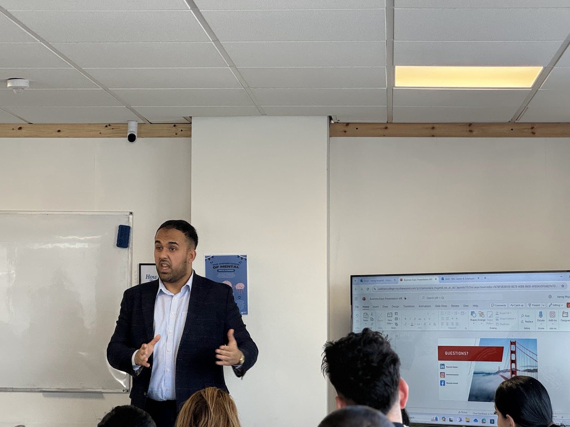 A presenter speaking to a seated audience at the WIC Business Expo, with a presentation screen behind him