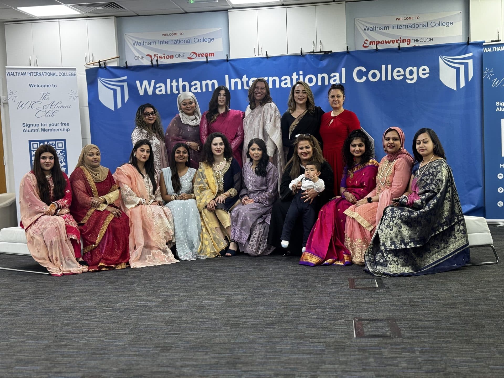A mixed group of students and staff in colourful traditional outfits posing together, London campus