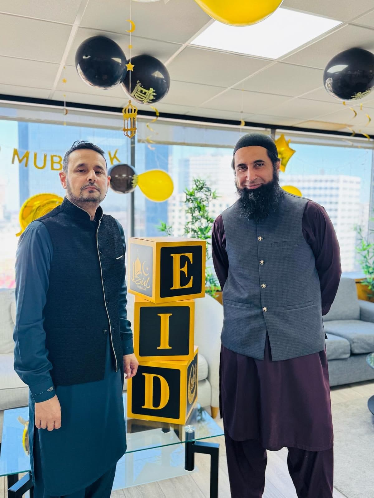 Two staff members beside stacked gold-and-black 'EID' letter blocks and balloons, Birmingham campus